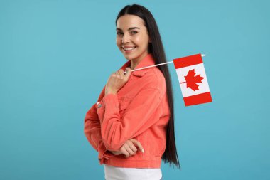 Açık mavi arka planda Kanada bayrağı taşıyan mutlu kadın