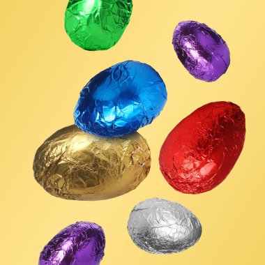 Parlak folyoyla çikolatalı yumurtalar pastel turuncu arka plana düşüyor.