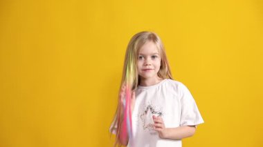 Renkli saç eklentileri olan gülümseyen kız sarı arka planda başparmak gösteriyor.