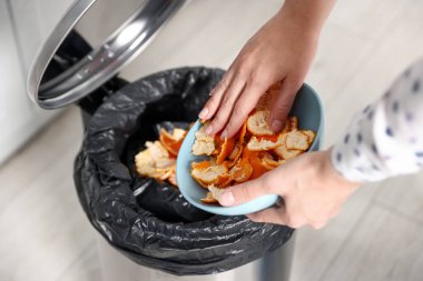 Mandalina kabuklarını mutfaktaki çöp kutusuna atan kadın, yakın plan.