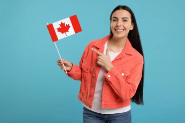 Açık mavi arka planda elinde Kanada bayrağını gösteren mutlu kadın.