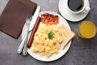 Lezzetli bir kahvaltı. Lezzetli çırpılmış yumurta, domuz pastırması, sosis ve ekmek gri desenli masada servis edilir.
