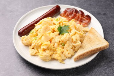 Lezzetli bir kahvaltı. Yağda yumurta, domuz pastırması, sosis ve ekmek. Gri desenli masada servis ediliyor. Yakın plan.