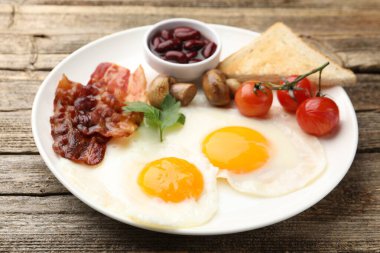 Geleneksel İngiliz kahvaltısı. Lezzetli, güneşli tarafı domuz pastırmalı, kırmızı fasulyeli, domatesli, mantarlı ve ahşap masada kızarmış ekmekli, yakın plan.