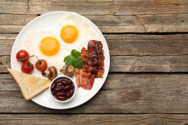 Geleneksel İngiliz kahvaltısı. Lezzetli, güneşli tarafı domuz pastırmalı, kırmızı fasulyeli, domatesli, mantarlı ve ahşap masadaki kızarmış ekmekli yumurtalar.