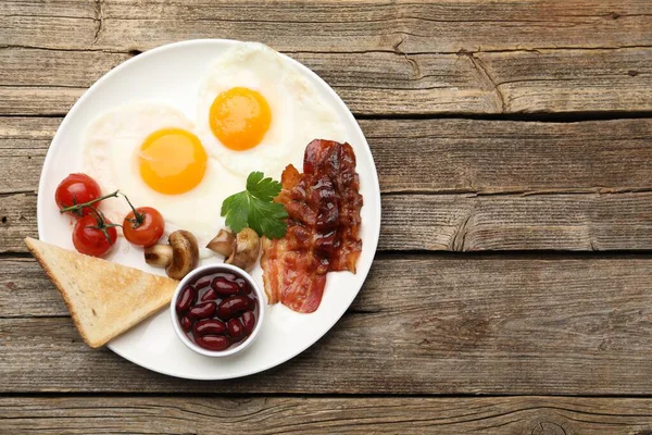 Geleneksel İngiliz kahvaltısı. Lezzetli, güneşli tarafı domuz pastırmalı, kırmızı fasulyeli, domatesli, mantarlı ve ahşap masadaki kızarmış ekmekli yumurtalar.