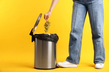 Sarı arka planda çöp kutusuna üzüm atan kadın, yakın plan.