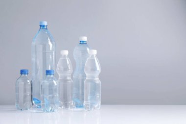 Beyaz masada gri arkaplan ile farklı boyutlarda su şişeleri, metin için boşluk