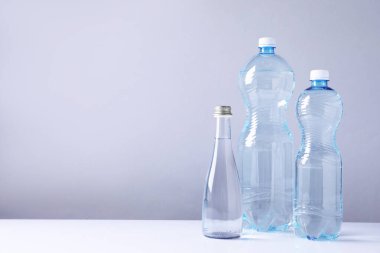 Beyaz masada gri arkaplan ile farklı boyutlarda su şişeleri, metin için boşluk