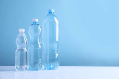 Beyaz masada açık mavi arka planda farklı boyutlarda su şişeleri var. Metin için boşluk