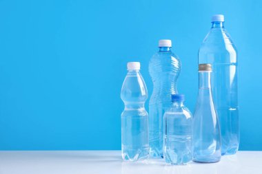 Beyaz masada farklı boyutlarda su şişeleri açık mavi arkaplan, metin için boşluk