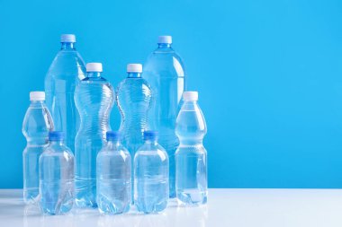 Beyaz masada farklı boyutlarda su şişeleri açık mavi arkaplan, metin için boşluk