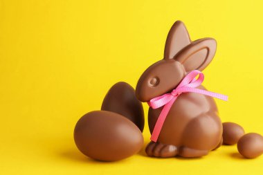Sarı arka planda çikolatalı Paskalya tavşanı ve yumurta. Metin için boşluk