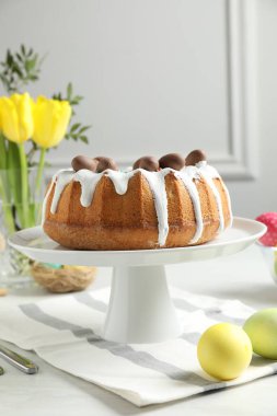 Lezzetli paskalya pastası, çikolatalı şekerler, boyanmış yumurtalar ve kapalı masa üzerinde sarı çiçekler, yakın plan.