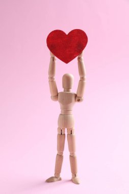 Pembe arka planda kırmızı kalpli tahta manken.