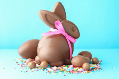 Çikolatalı Paskalya tavşanı, yumurtalar, şekerler ve açık mavi arka planda serpiştirmeler.