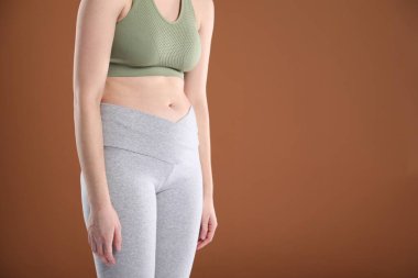 Spor giyinen, kahverengi arka planda kötü duruşu olan bir kadın, yakın plan. Metin için boşluk