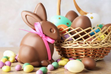 Çikolatalı Paskalya tavşanı ve hasır sepetteki yumurtalar ahşap masada açık gri arka planda, yakın plan
