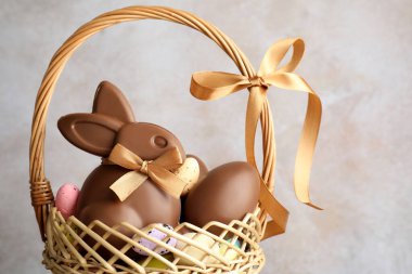 Çikolatalı Paskalya tavşanı ve hasır sepette yumurtalar açık gri arka planda, yakın plan.