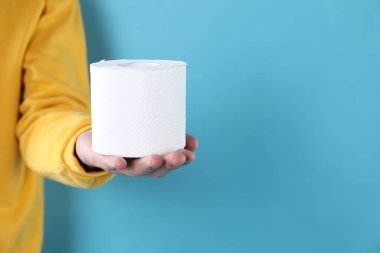 Açık mavi arka planda tuvalet kağıdı rulosu olan adam, yakın plan. Metin için boşluk