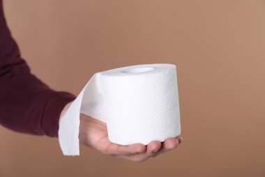 Koyu bej arka planda tuvalet kağıdı rulosu olan adam, yakın plan. Metin için boşluk