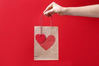 Kırmızı arka planda kalbi olan hediye paketi tutan kadın, yakın plan. Sevgililer Günü