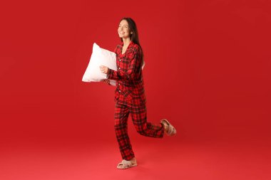 Kırmızı arka planda yastıklı şık pijamalı mutlu kadın.