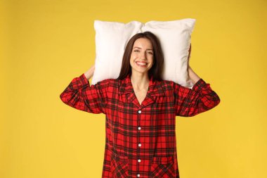 Sarı arka planda yastıklı şık pijamalı mutlu kadın.