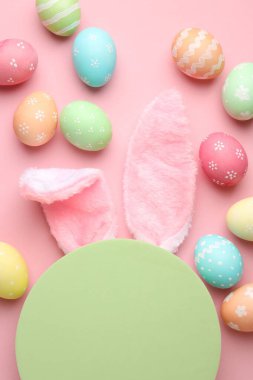 Mutlu Paskalyalar. Şirin tavşan kulakları, boyalı yumurtalar ve pembe arka planda boş podyum, düz uzanma.