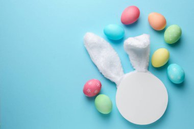 Mutlu Paskalyalar. Şirin tavşan kulakları, boş podyum ve açık mavi arka planda boyanmış yumurtalar, düz yatak. Metin için boşluk