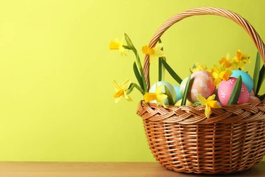 Boyanmış Paskalya yumurtaları ve ahşap masada açık yeşil arka planda hasır sepetteki güzel nergisler, yakın plan. Metin için boşluk