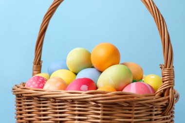 Hasır sepette boyalı Paskalya yumurtaları açık mavi arkaplan, yakın plan.