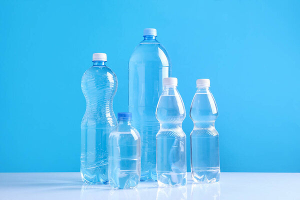 Water bottles of different sizes on white table against light blue background