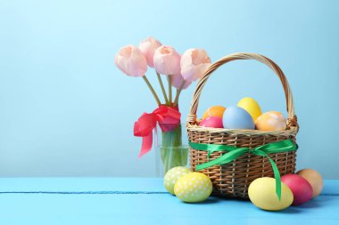 Hasır sepete boyanmış Paskalya yumurtaları ve açık mavi arka plana karşı ahşap masada güzel laleler. Metin için boşluk