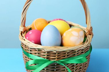 Hasır sepete boyanmış Paskalya yumurtaları açık mavi arkaplanda, yakın plan.