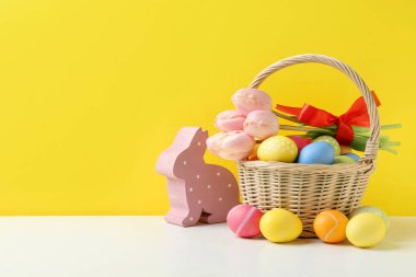Hasır sepette güzel lalelerle boyanmış Paskalya yumurtaları ve sarı arka planda beyaz masa üzerine dekoratif tavşancık. Metin için boşluk