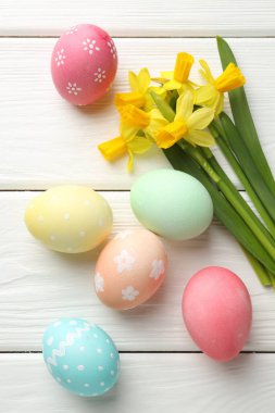 Boyanmış Paskalya yumurtaları ve beyaz ahşap masa üzerinde güzel nergisler.