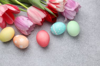 Boyanmış Paskalya yumurtaları ve gri desenli masa üzerinde güzel laleler.
