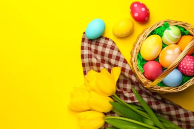 Sarı arka planda boyanmış yumurta ve lalelerin olduğu Paskalya sepeti, düz. Metin için boşluk