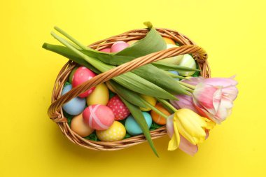 Sarı arka planda boyanmış yumurtalar ve laleler olan Paskalya sepeti.