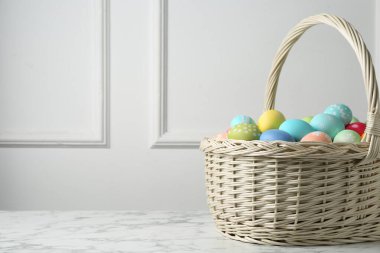 Hasır sepete boyanmış Paskalya yumurtaları beyaz duvarın yanındaki beyaz mermer masada. Metin için boşluk