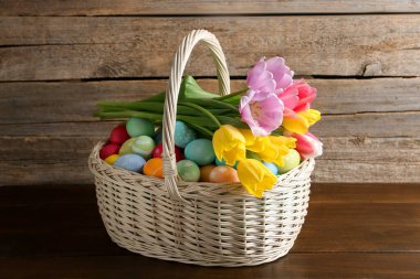 Hasır sepete boyanmış Paskalya yumurtaları ve ahşap masada güzel laleler.