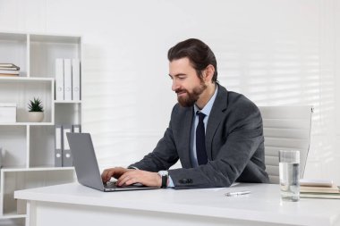 Beyaz duvarın yanındaki masada dizüstü bilgisayarla çalışan bir iş adamı.