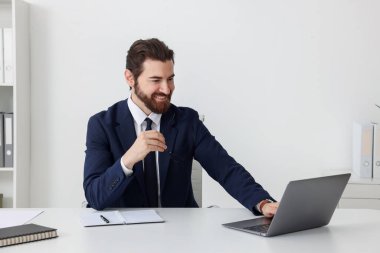 Beyaz duvarın yanındaki masada dizüstü bilgisayarla çalışan bir iş adamı.