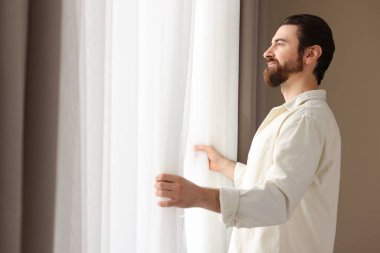 Evde şık pencere perdeleri açan adam