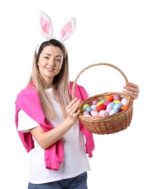 Paskalya kutlaması. Saç bandı takmış, tavşan kulaklı, hasırdan sepet dolusu beyaz arka planda boyalı yumurtaları olan gülümseyen bir kadın.