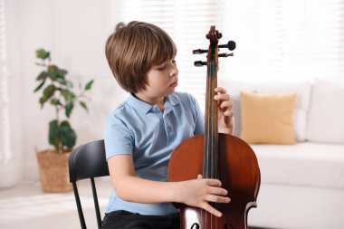 Evdeki sandalyede keman çalan küçük çocuk.