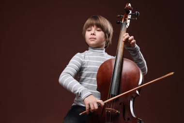 Kahverengi arka planda keman çalan sevimli küçük çocuk, metin için yer var.