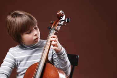 Kahverengi arka planda keman çalan sevimli küçük çocuk, metin için yer var.