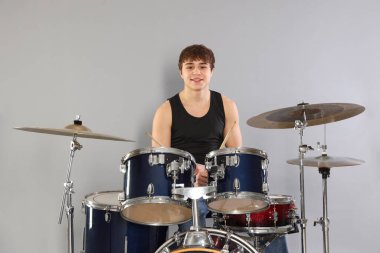 Gri arka planda davul çalmayı öğrenen güler yüzlü genç çocuk.